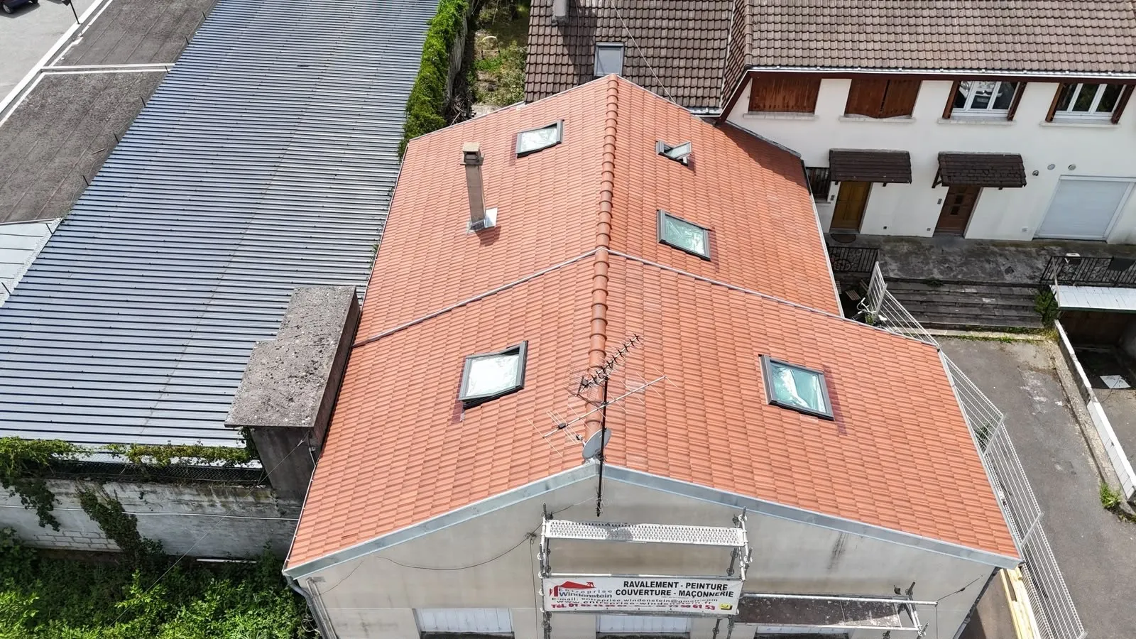 Vue aérienne d’une toiture en tuiles orangées avec fenêtres de toit et cheminée.